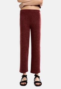 Czerwone, teksturowane spodnie o prostym kroju i wygodnym pasie, połączone z czarnymi sandałami na pasku z złotym akcentem.