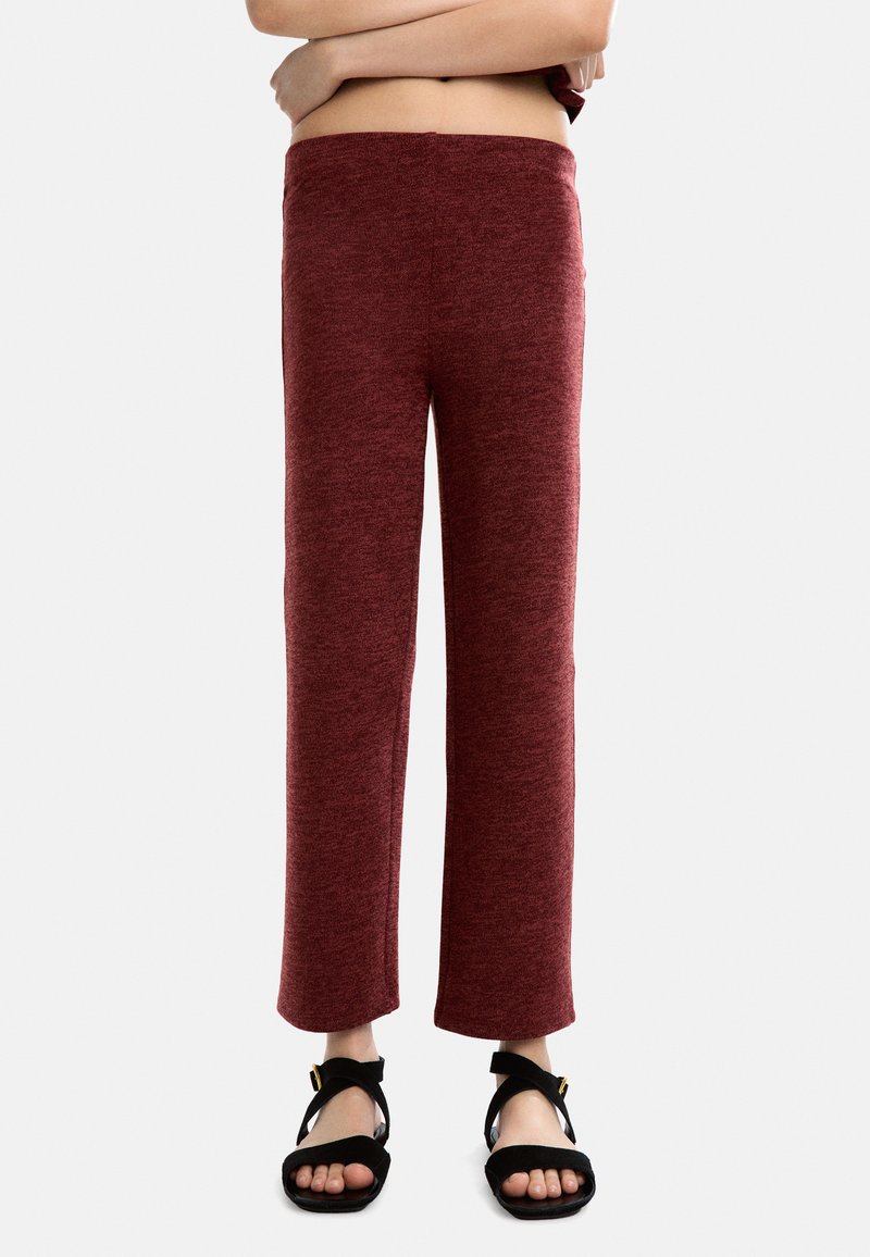 Czerwone, teksturowane spodnie o prostym kroju i wygodnym pasie, połączone z czarnymi sandałami na pasku z złotym akcentem.