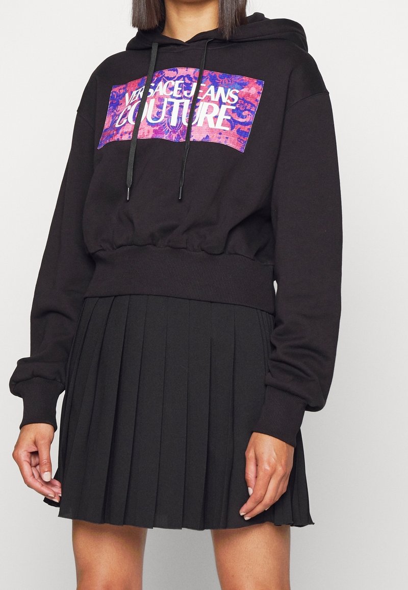 Černá zkrácená mikina s grafickým potiskem, s kapucí na šňůrku a žebrovaným lemem. Kombinována se skládací černou sukní.