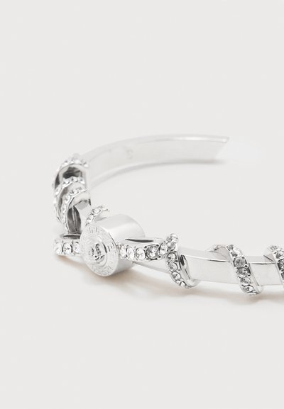 Ασημένιο βραχιόλι μανσέτα με διαφανή στρας που τυλίγονται γύρω και κυκλικό διακοσμητικό κούμπωμα.