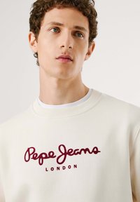 Sudadera crema con cuello acanalado y bordado en burdeos "Pepe Jeans London". Presenta una textura suave y un corte clásico.