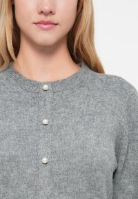 Γκρι πλεκτό ζακέτα με στρογγυλή λαιμόκοψη, τρία κουμπιά πέρλες μπροστά και μαλ�ακό, υφασμάτινο υλικό.
