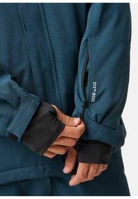 Türkisfarbene Außenjacke mit einer Reißverschlusstasche am Ärmel. Verfügt über schwarze Bündchen und einen Klettverschluss, hergestellt aus hochwertigem Stoff für den Einsatz im Freien.