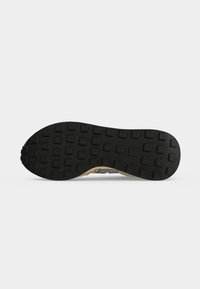Semelle de chaussure avec une bande de roulement en caoutchouc noir comportant des clous carrés disposés en rangées pour une meilleure traction sur une semelle beige.
