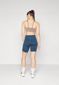 Brun sports-bh med justerbare stropper kombinert med mørkeblå høytalgende sykkelshorts. Hvite sokker og joggesko fullfører antrekket.