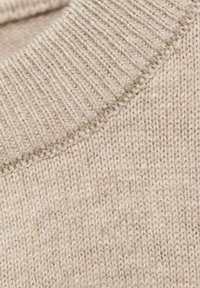 Bežová pletenina s texturovaným, žebrovaným výstřihem. Vzor má jemnou, hladkou strukturu s jednotným designem stehu.