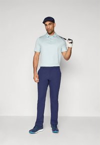 Ανοιχτό μπλε πόλο πουκάμισο, σκουρό μπλε παντελόνι και σκουρό μπλε παπούτσια. Το άτομο κρατάει μπαστούνι του γκολφ με γαντζωμένο χέρι. Φοράει σκουρό μπλε καπέλο.