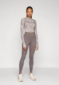 Szary krótki top z długim rękawem w wzór imitujący skórę węża, dopasowane szare legginsy z przeszyciami podkreślającymi kontury, do tego jasne trampki z logo.