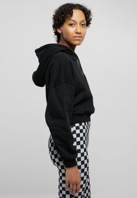 Svart cropped hoodie med snøring, kombinert med høyt liv svarte og hvite rutete leggings. Glatt stoff, avslappet passform.