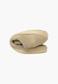 Zapatos beige tipo slip-on con parte superior de ante suave y suela de goma lisa, que cuentan con una punta redonda y un diseño plegado para un almacenamiento compacto.