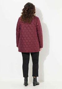 Bordeaux gewatteerde jas met een lange, relaxte pasvorm, voorzien van een ruitpatroon. Gekleed met zwarte slim-fit broek en enkellaarsjes.