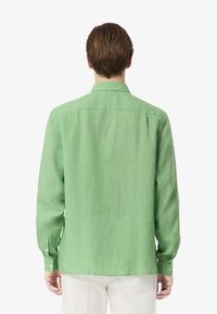 Camicia di lino verde con colletto, maniche lunghe e polsini con bottone, caratterizzata da una superficie leggermente texture e una vestibilità morbida.