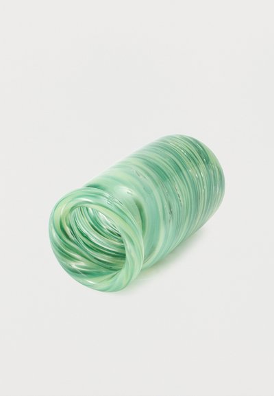 Διάφανο πράσινο γυάλινο βάζο με σπειροειδή σχέδια, που βρίσκεται στο πλάι σε λευκό φόντο.