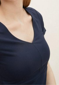 Mörkblå V-ringad topp i ett mjukt bomullsblandningsmaterial, med korta ärmar och subtila sömnadsdetaljer längs sömmarna.