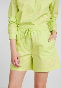 Light green shorts made of a smooth fabric. Features an elastic waistband with a drawstring and side pockets. Short length, casual design.
