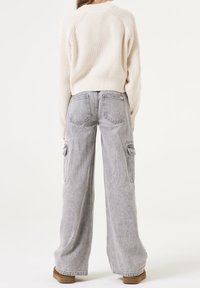 Pull crème côtelé à manches longues associé à un jean cargo gris à taille haute, large, avec poches latérales et une légère texture.