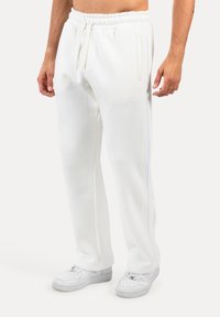 Weiße Fleece-Jogginghose mit elastischem Bund, Kordelzug, Seitentaschen und einem dezenten Logo. Glatte Textur mit geradem Bein. 