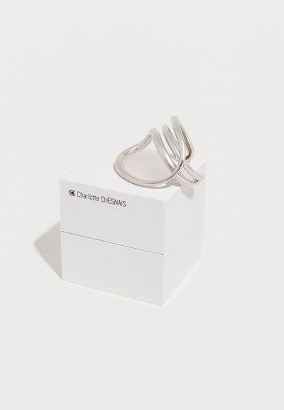 Ασημένιο αφηρημένο κυρτό δαχτυλίδι, το οποίο ακουμπά πάνω σε ένα λευκό κουτί δύο τεμαχίων με την επιγραφή "Charlotte CHESNAIS" τυπωμένη μαύρα στο πάνω τμήμα.