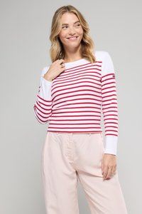Haut à manches longues avec des rayures horizontales rouges et blanches, un col rond et des manches blanches unies en contraste. Porté avec un pantalon rose clair.