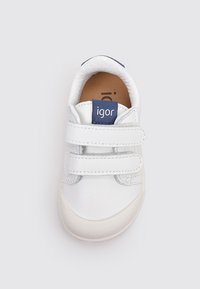Zapatillas blancas para niños con dos correas de velcro, punta redondeada y una etiqueta azul marino con "igor". Material de cuero suave con un forro blando.