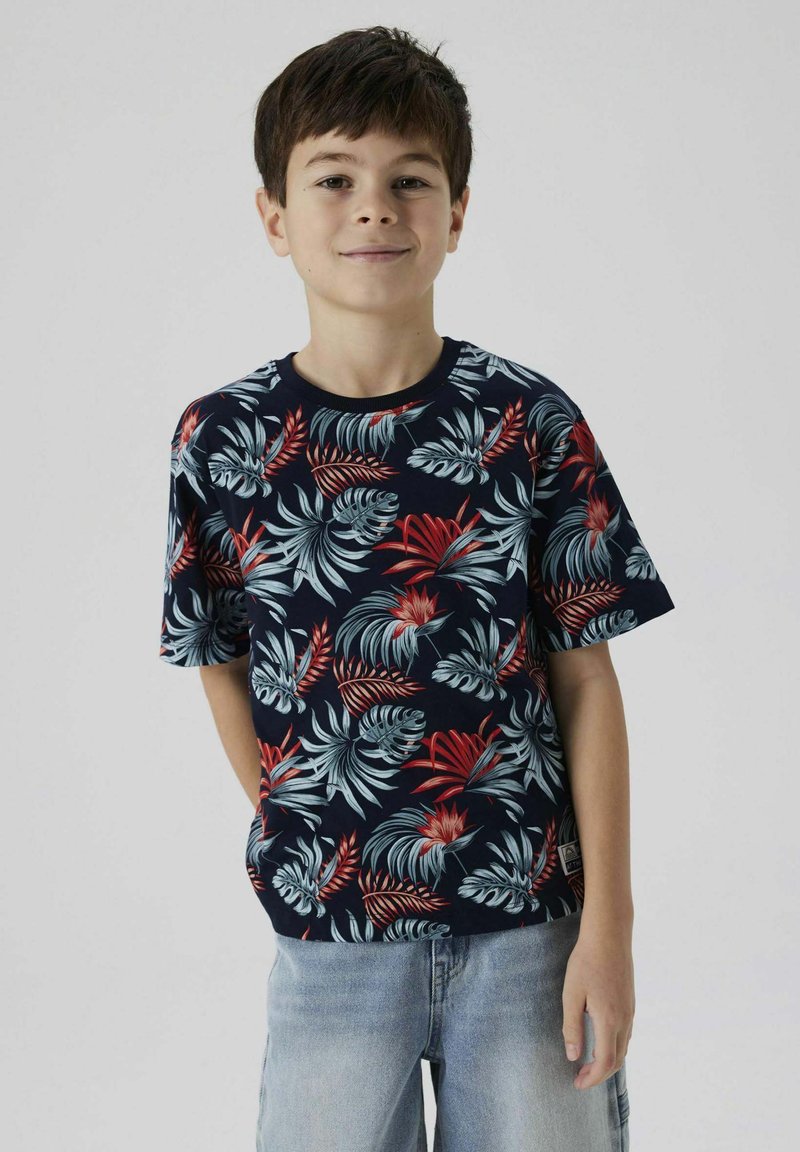 Camiseta de manga corta en color marino con un patrón de hojas tropicales en rojo y azul claro. Hecha de una tela suave con un corte holgado.