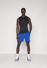 Mustat ilmanhihoittomat urheilupaidat, joissa on valkoinen Nike-logo, yhdistettynä sinisiin shortseihin, joissa on valkoisella tekstillä "DODGERS". Harmaat urheilukengät.