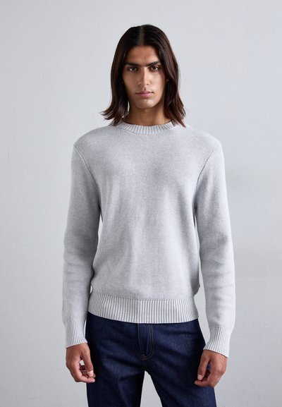 Maglione grigio chiaro a maglia con collo a giro, polsini e orlo a coste, indossato da un modello su uno sfondo neutro.