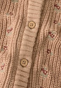 Strikket cardigan i myk beige med ribbestruktur. Har blomsterbroderi i dempede farger og tre treknapper.