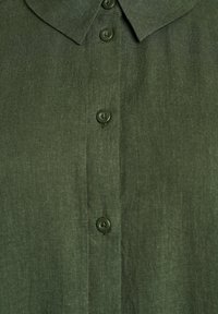 Tmavozelená košeľa na zapínanie s golierom, zobrazujúca tri gombíky na prednej strane na textúrovanom materiáli.