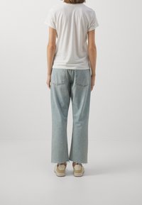 Bílé tričko s krátkým rukávem spárované se světle modrými širokými džínami s třepenými lemy a dvěma zadními kapsami. Outfit doplňují béžové tenisky.