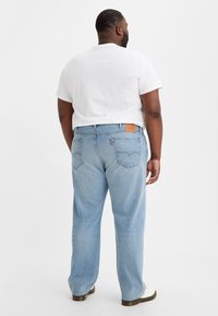 Jeans in denim azzurro chiaro con vestibilità comoda, dotati di tasche posteriori e una patch in pelle vicino alla vita. Abbinati a una t-shirt bianca.