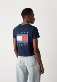 Marineblå cropped t-shirt lavet af bomuld, med et grafisk design bestående af røde, hvide og blå rektangler samt teksten "TOMMY JEANS" på ryggen.