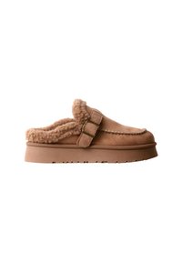 Chaussure slip-on en daim brun clair avec doublure en shearling et sangle ajustable avec boucle en laiton sur semelle épaisse, vue de côté sur fond blanc.