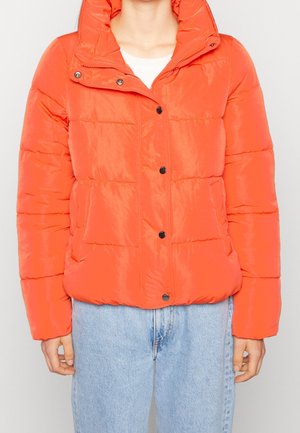 Feloranje donsjack met drukknopen en zijzakken, gedragen over een wit topje en lichtblauwe spijkerbroek.