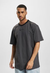 Gray cotton t-shirt with short sleeves, black ribbed neckline, and embroidered detail on the chest. Loose-fitting design.