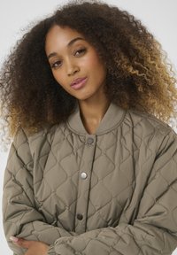 Veste bombardier matelassée vert olive avec un col rond, des boutons-pression et des poignets élastiques, arborant un motif de losanges texturé.