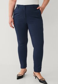 Mørkeblå skræddersyede bukser med en glat overflade, der har flad front, sidelommer og et slim fit. Båret med sorte spidse hæle.