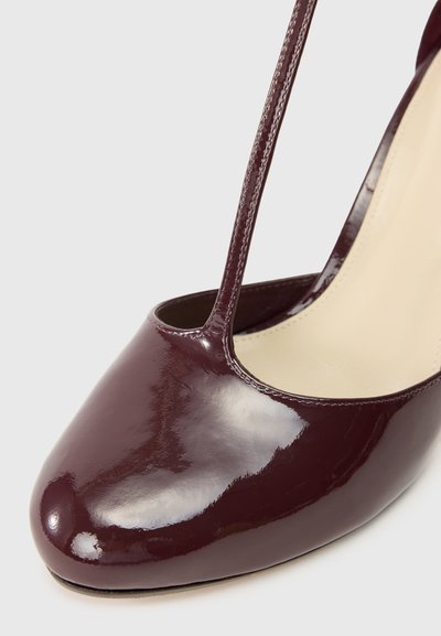 Μπορντό παπούτσι με τακούνι από πατεντέ δέρμα, με τελείωμα σε αιχμή, που διαθέτει ανοιχτή πλευρά και λεπτές αλυσίδες στήριξης. Λείο, γυαλιστ�ερό υλικό.