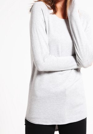 Maglietta a maniche lunghe grigia chiara con collo a giro, realizzata in tessuto morbido. Presenta una vestibilità rilassata e un orlo posteriore leggermente allungato.