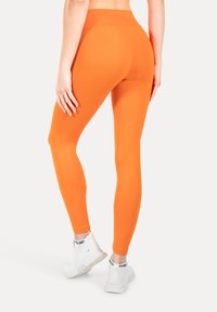 Oranje leggings van glad, rekbaar materiaal met een hoge tailleband, gecombineerd met witte sportschoenen met zwarte accenten.