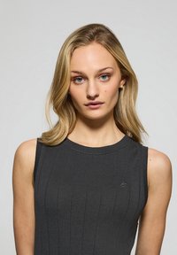 Ärmlös ribbad linne i mörkgrått med rund halsringning och subtil logotypdetalj. Slät textur med en figurnära passform.