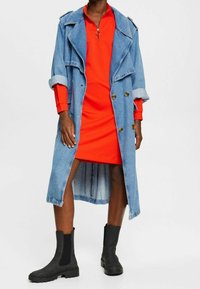 Dżinsowy trencz nałożony na czerwoną sukienkę z zamkiem przy kołnierzu. Czarne botki za kostkę z elastycznymi panelami bocznymi. Cecha podwójnie zapięty przód.