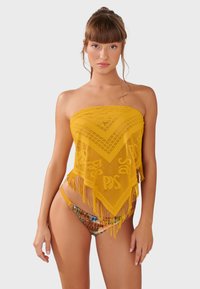 Žltý háčkovaný bandeau top s trojuholníkovým vzorom a strapcami. Kombinovaný s farebnými bikinovými spodkami s kvetinovým vzorom.