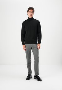 Schwarzer Rollkragenpullover mit langen Ärmeln, kombiniert mit hellgrauen, maßgeschneiderten Hosen und glänzenden schwarzen Schuhen. Einfaches Design, strukturierter Stoff.