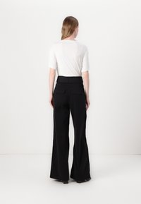 Zwarte wijde broek met hoge taille, twee achterzakken en een gladde, gestructureerde afwerking; gecombineerd met een eenvoudig wit t-shirt met korte mouwen.