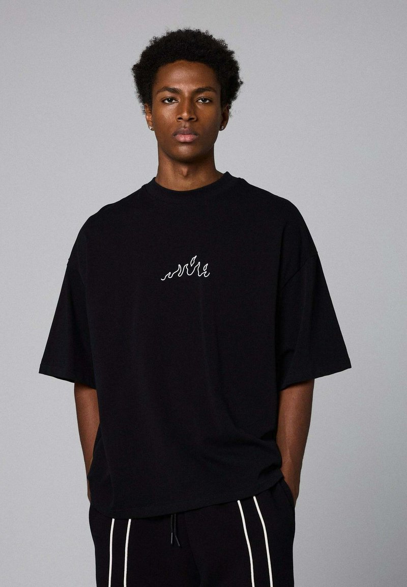 Schwarzes, übergroßes T-Shirt aus Baumwolle mit einem weißen Wellenmuster-Logo auf der Brust und kurzen Ärmeln. Einfaches, ungeschmücktes Design.