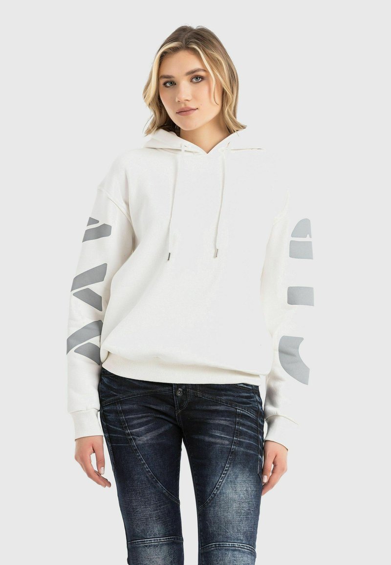 White hoodie with gray graphic accents on sleeves, drawstrings, and ribbed hem. Paired with dark blue distressed jeans.
