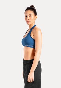 Blauwe geribbelde sportbeha met racerback ontwerp en witte logodetail. Gecombineerd met zwarte broek met elastische taille. Gladde, aansluitende textuur.