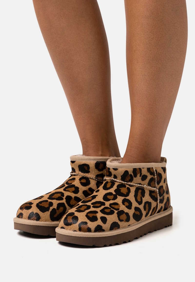 Botas de tobillo de estampado de leopardo en tonos marrón y negro, con una textura suave y puntera redondeada, un cuello beige y suela de goma para mayor tracción.