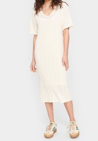 Knit midi-mekko off-white-värissä, jossa on V-pääntie ja lyhyet hihat, sekä teksturoitu pinta. Yhdistetty rentoihin monivärisiin lenkkareihin.